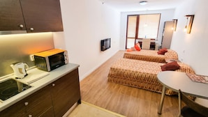 A compact hotel room with a kitchenette, two beds with patterned bedding, a small dining table, and a TV mounted on the wall. - Mountain Paradise 2 - Quiet Cosy Studio - Balcony, Wifi (Bansko)