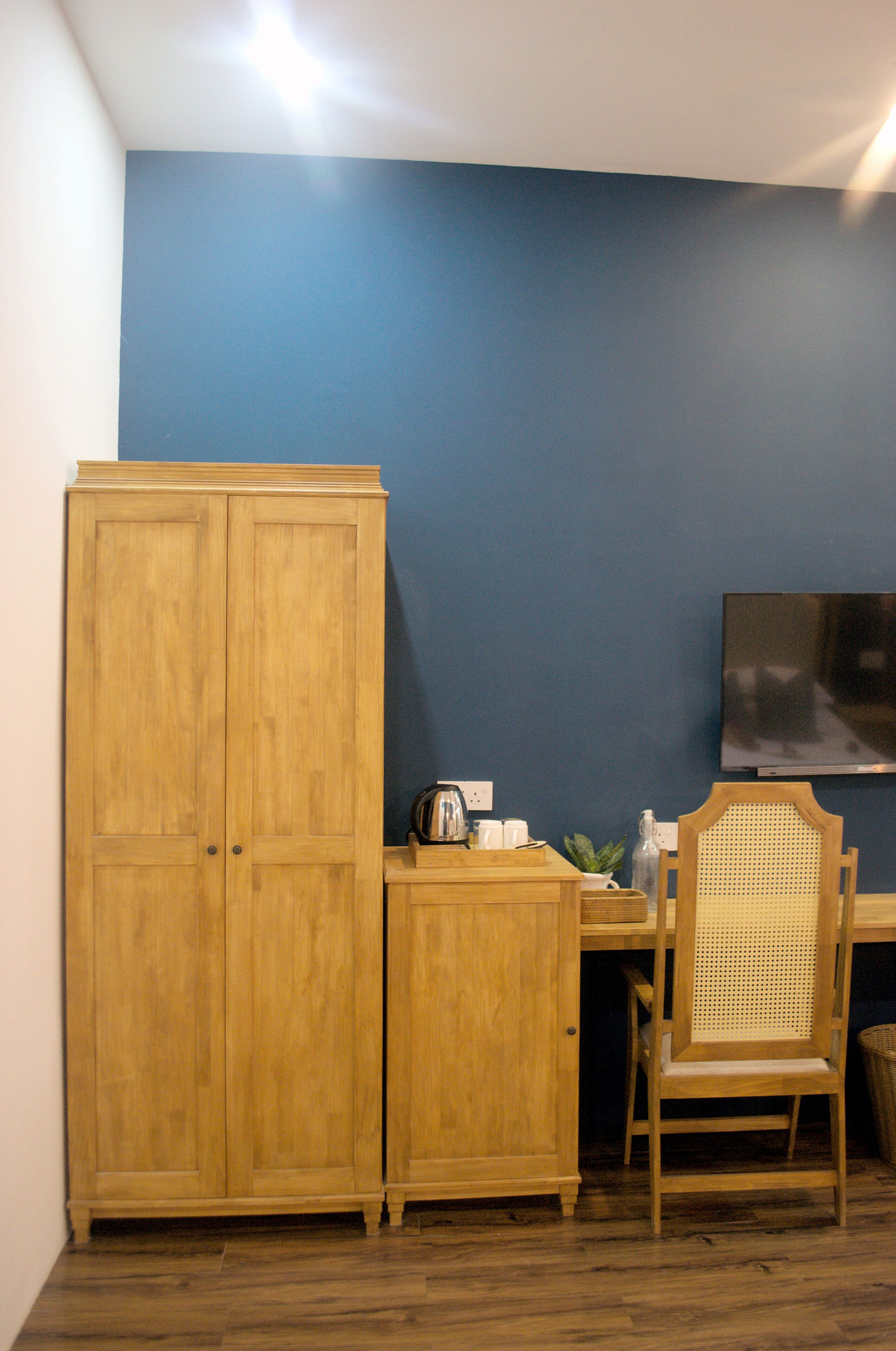 A room with a wooden wardrobe, a desk with a chair, a television, and a small plant.