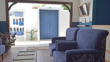 A room with two blue armchairs, a wooden floor, a blue door, and a wall-mounted mirror.