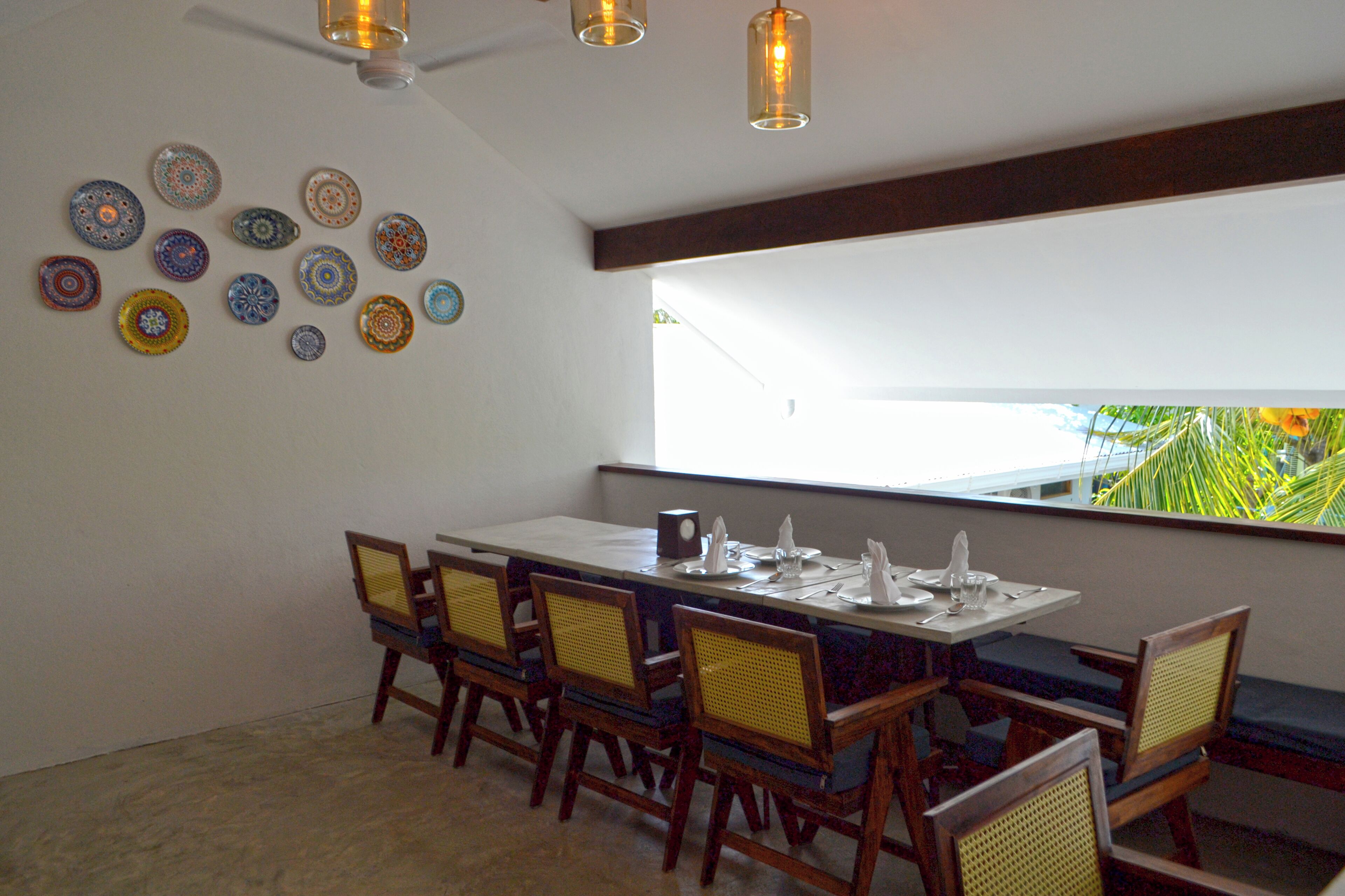 A dining area with a long table set for six, surrounded by wooden chairs with woven seats.