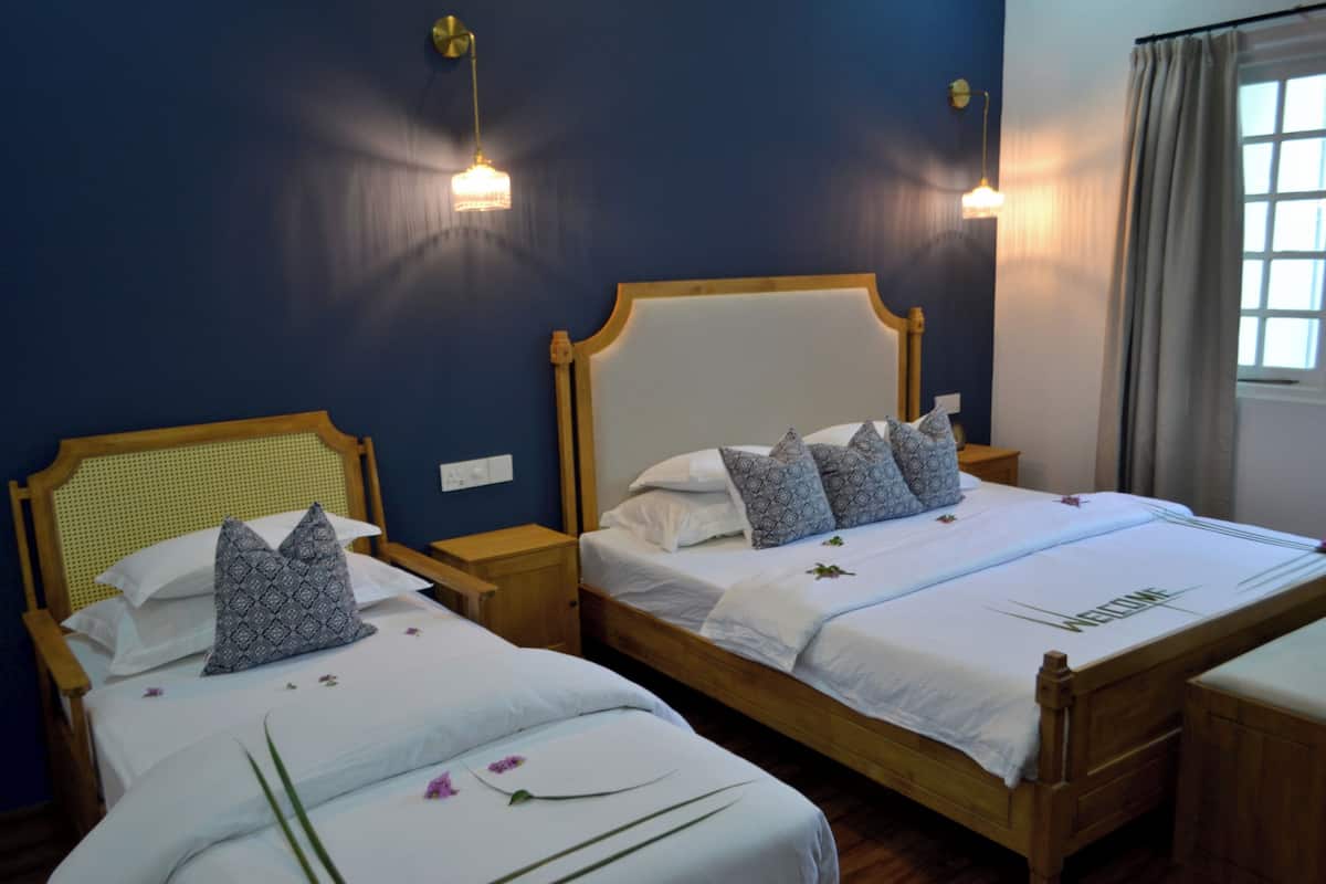 Two single beds with wooden frames and white bedding, a nightstand between them, and a window with curtains to the right.