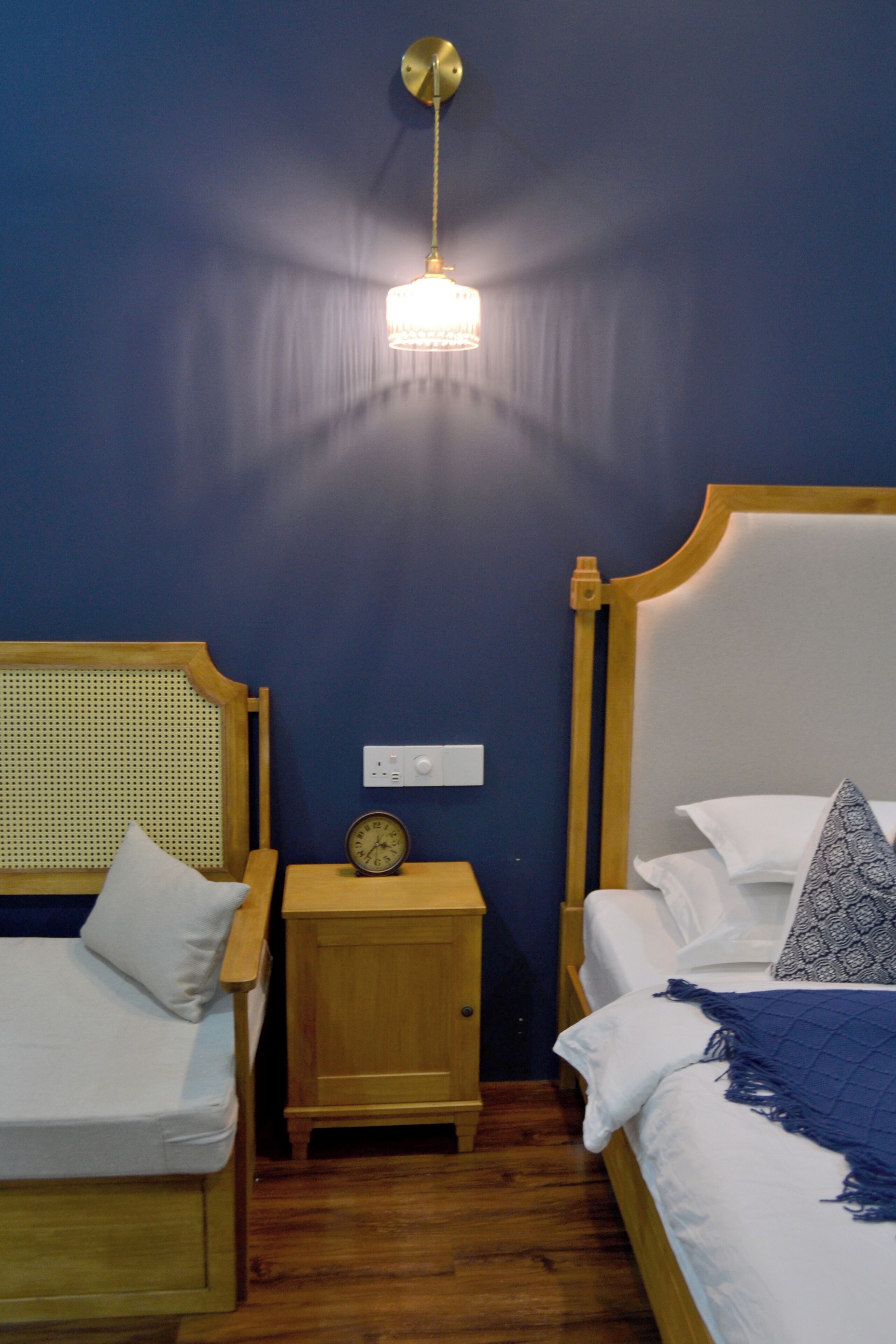 A room with two wooden beds, a nightstand with a clock, and a hanging light fixture.