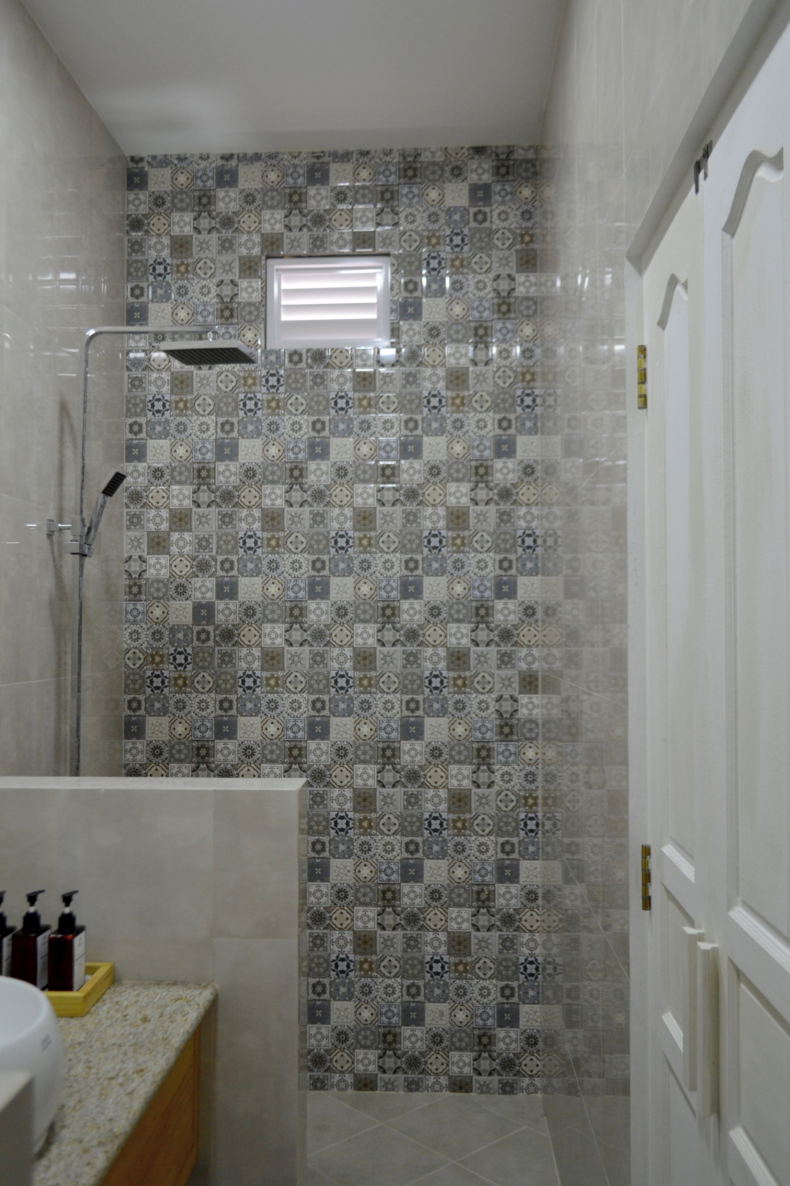A bathroom with a tiled shower wall, a handheld showerhead, and a small window.