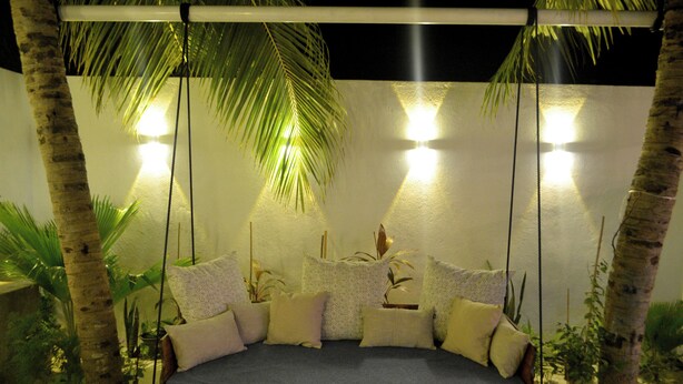 A cozy outdoor seating area with a swing bed, surrounded by palm trees and potted plants, under ambient lighting. - Athirige Boutique House (Dharavandhoo)