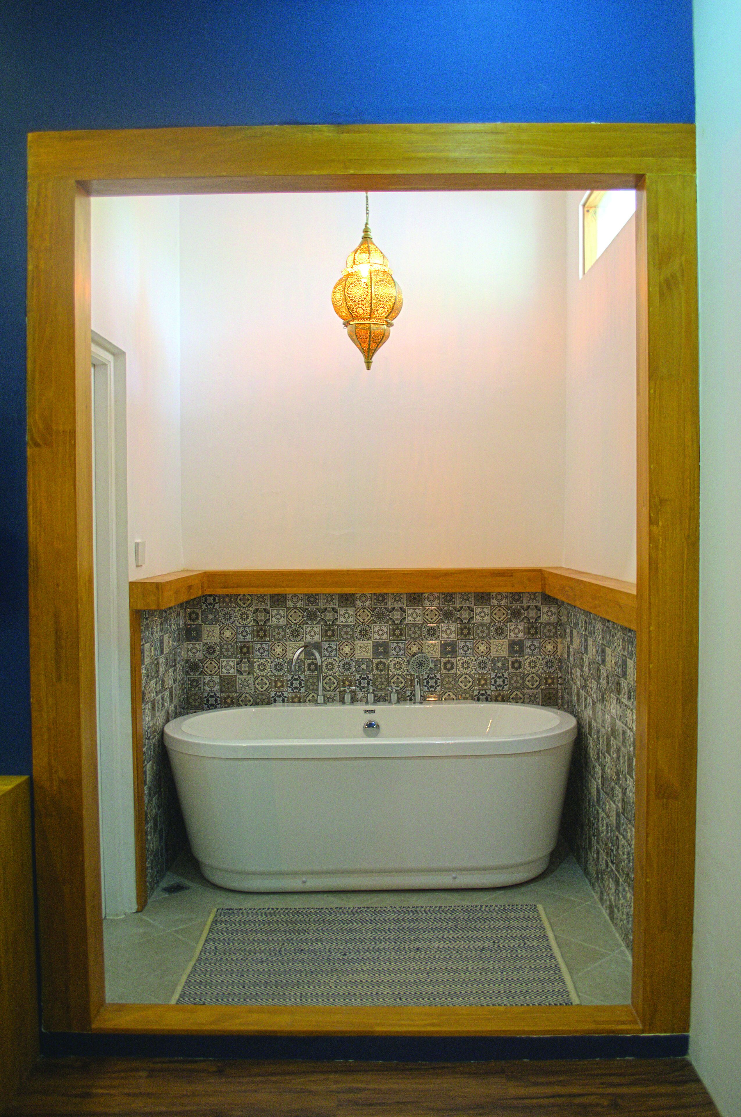 Un baño con una bañera independiente, un salpicadero de azulejos estampados y una lámpara colgante.