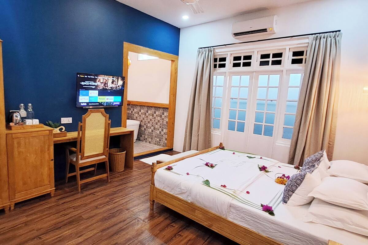 A bedroom with a bed, wooden wardrobe, desk, chair, and a TV on the wall.
