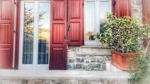 A stone building with red shutters and a potted plant on the windowsill.