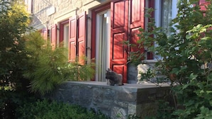 A stone building with red shutters and a cat statue on the porch.
