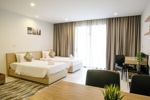 Two single beds with white linens and matching pillows, a desk, and a potted plant.