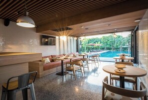 Relax in a spacious room with a long bench and dining tables, surrounded by lush views of the outdoor area and pool.