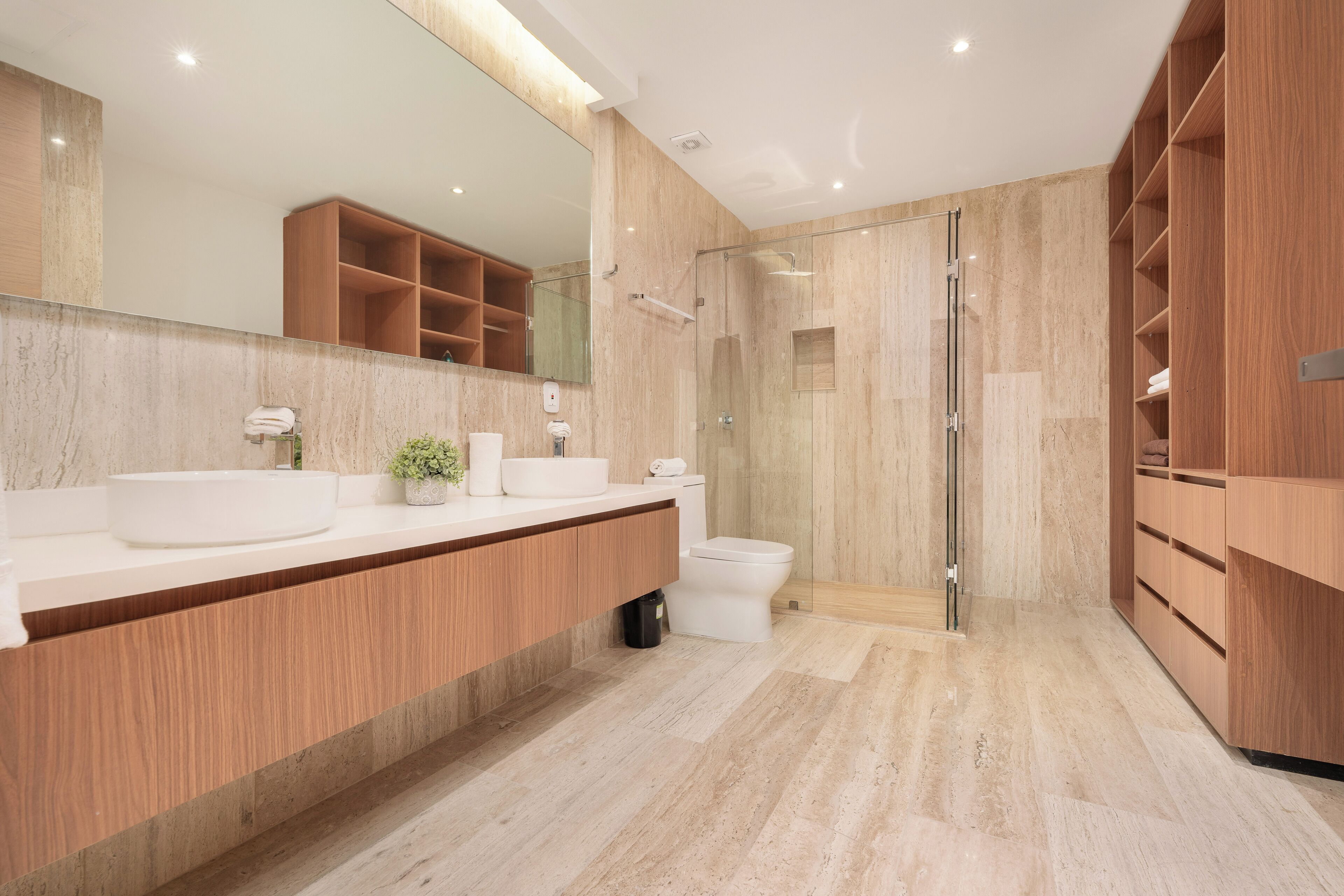 Une salle de bain moderne dotée d’un grand miroir, de deux lavabos, de toilettes et d’une douche à l’italienne.
