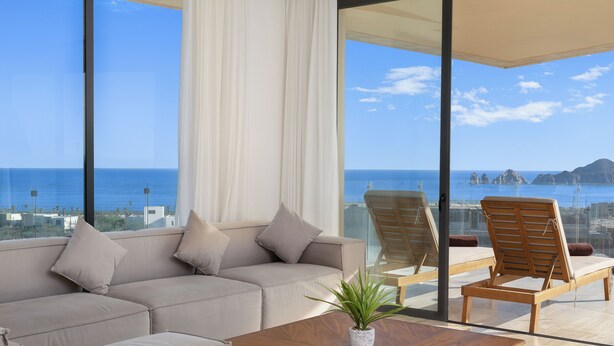A modern living room with a sofa, chairs, and a coffee table. Large windows offer a view of the sea and distant islands. - Mistiq Los Cabos  (Cabo San Lucas)