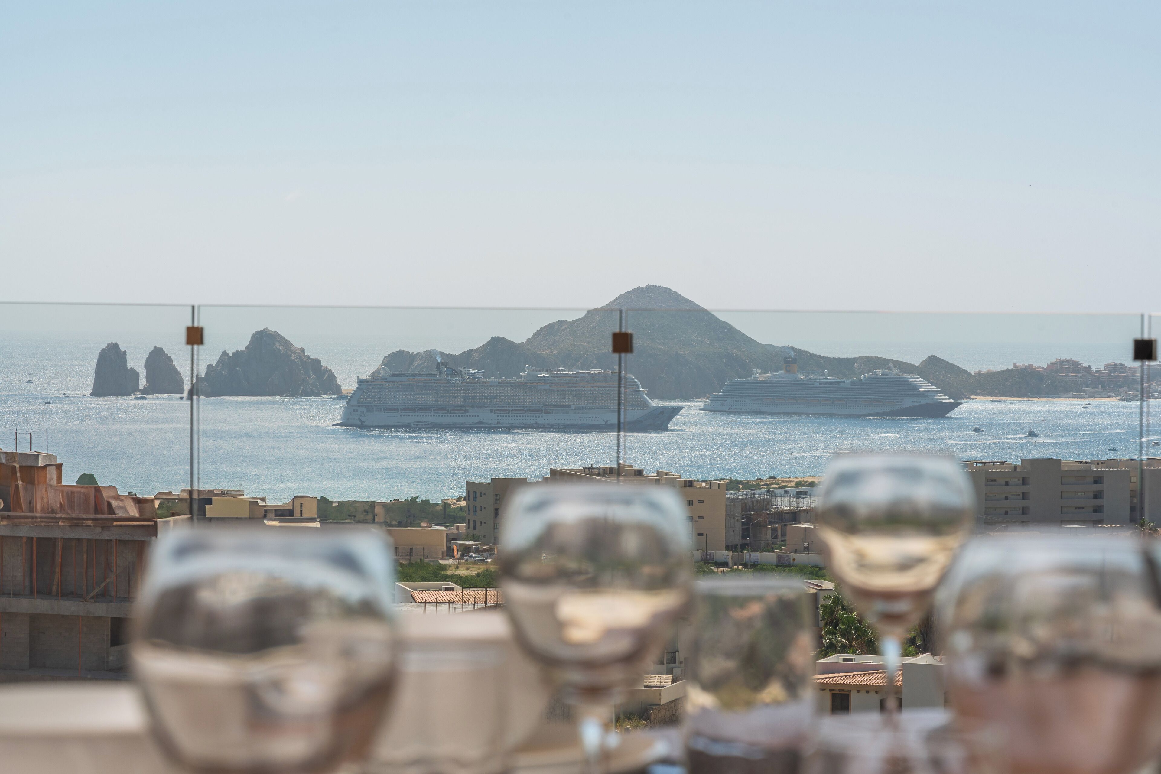 A view from a balcony overlooking a coastal area with ships in the distance and several glasses of wine in the foreground.