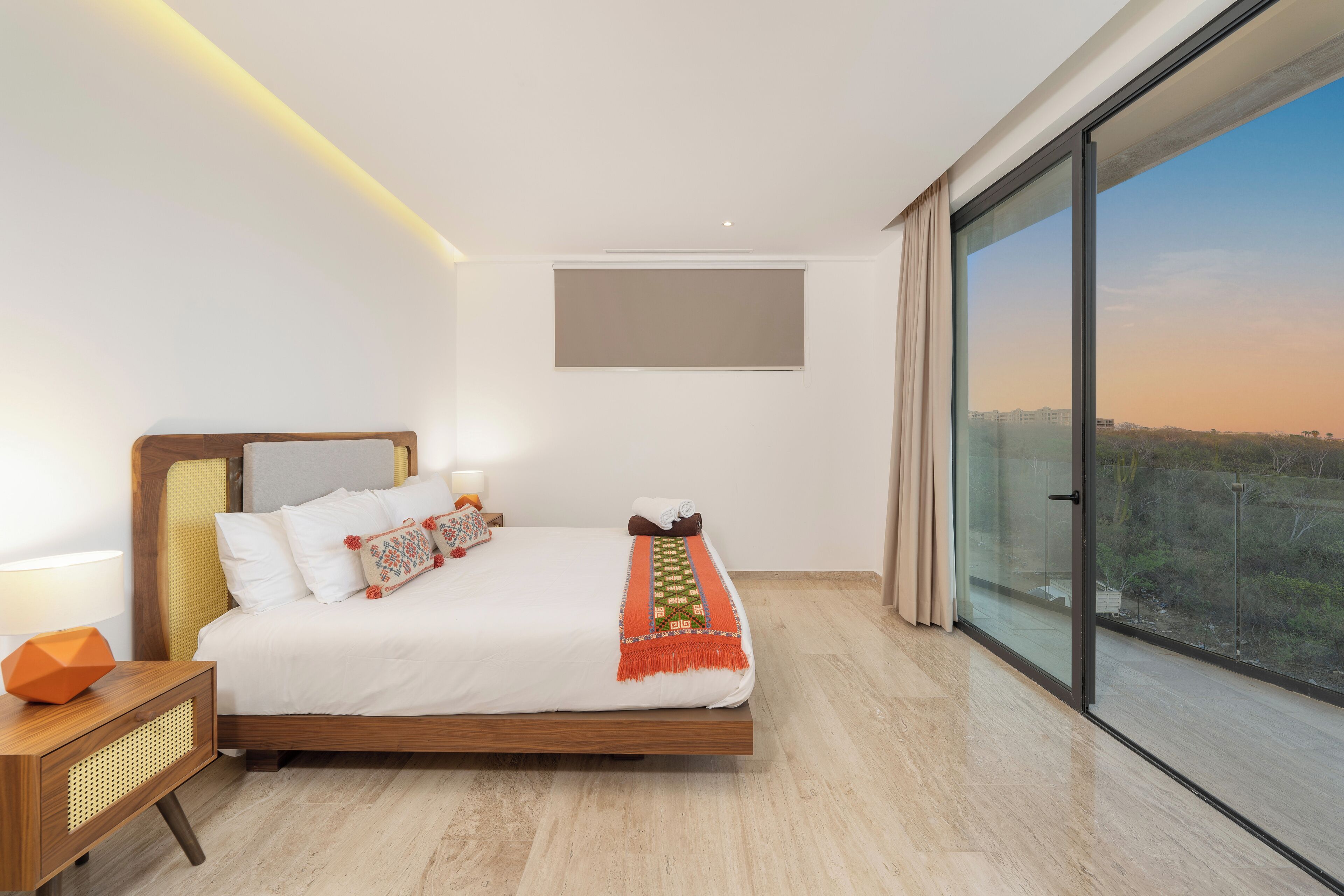 Een moderne slaapkamer met een groot bed, bedlampen, een nachtkastje en een uitzicht door een groot raam.