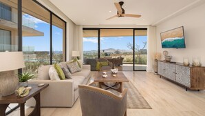 A spacious living room with a large window, a ceiling fan, a sofa, a coffee table, and a cabinet. - Mistiq Los Cabos  (Cabo San Lucas)