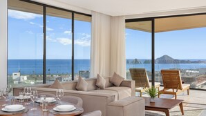 A modern hotel room with a large balcony, a sofa, a dining table set, and a view of the sea and cityscape. - Mistiq Los Cabos  (Cabo San Lucas)