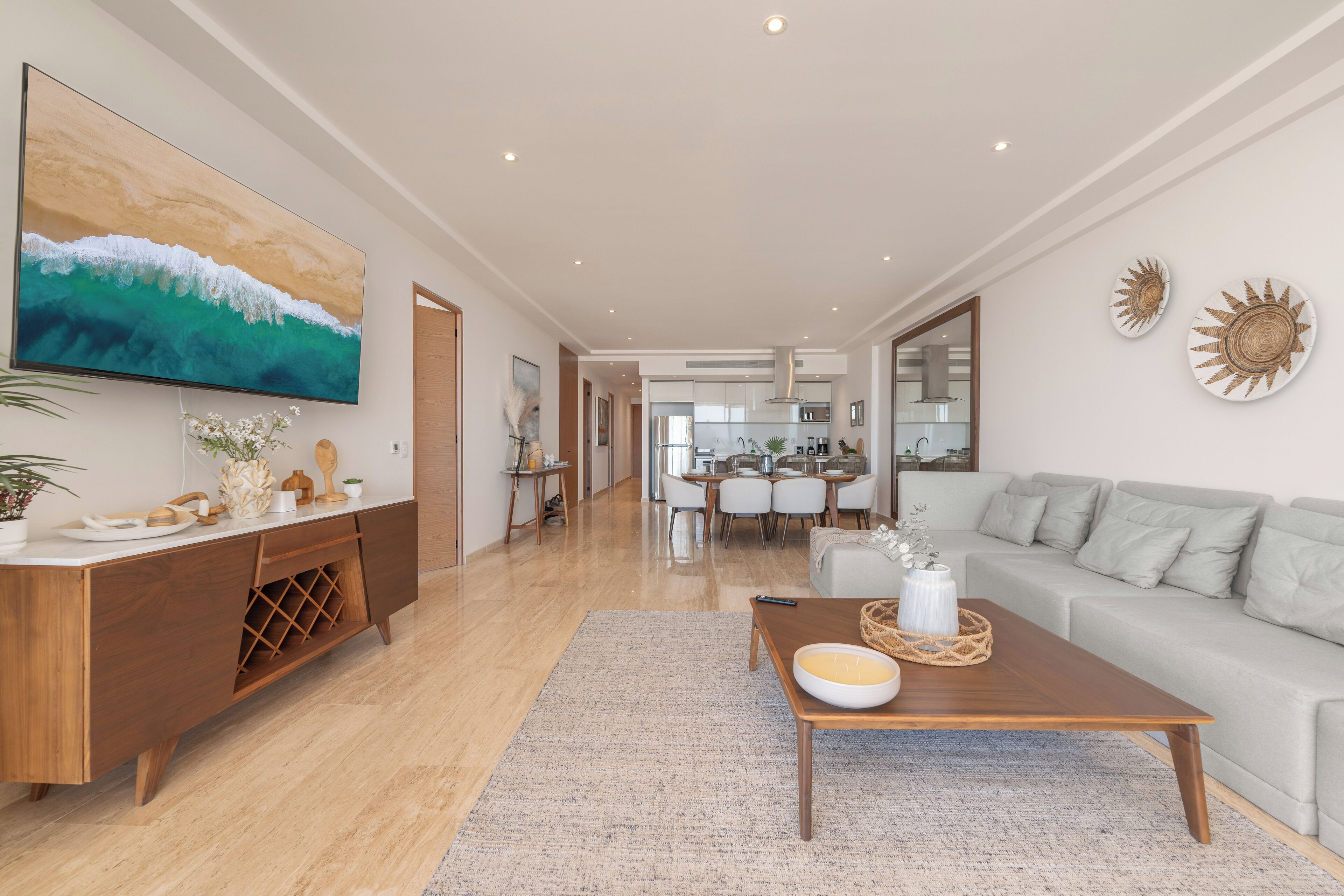 Uma sala de estar moderna com uma mesa de centro de madeira, um sofá cinza e uma televisão de tela plana fixada na parede.