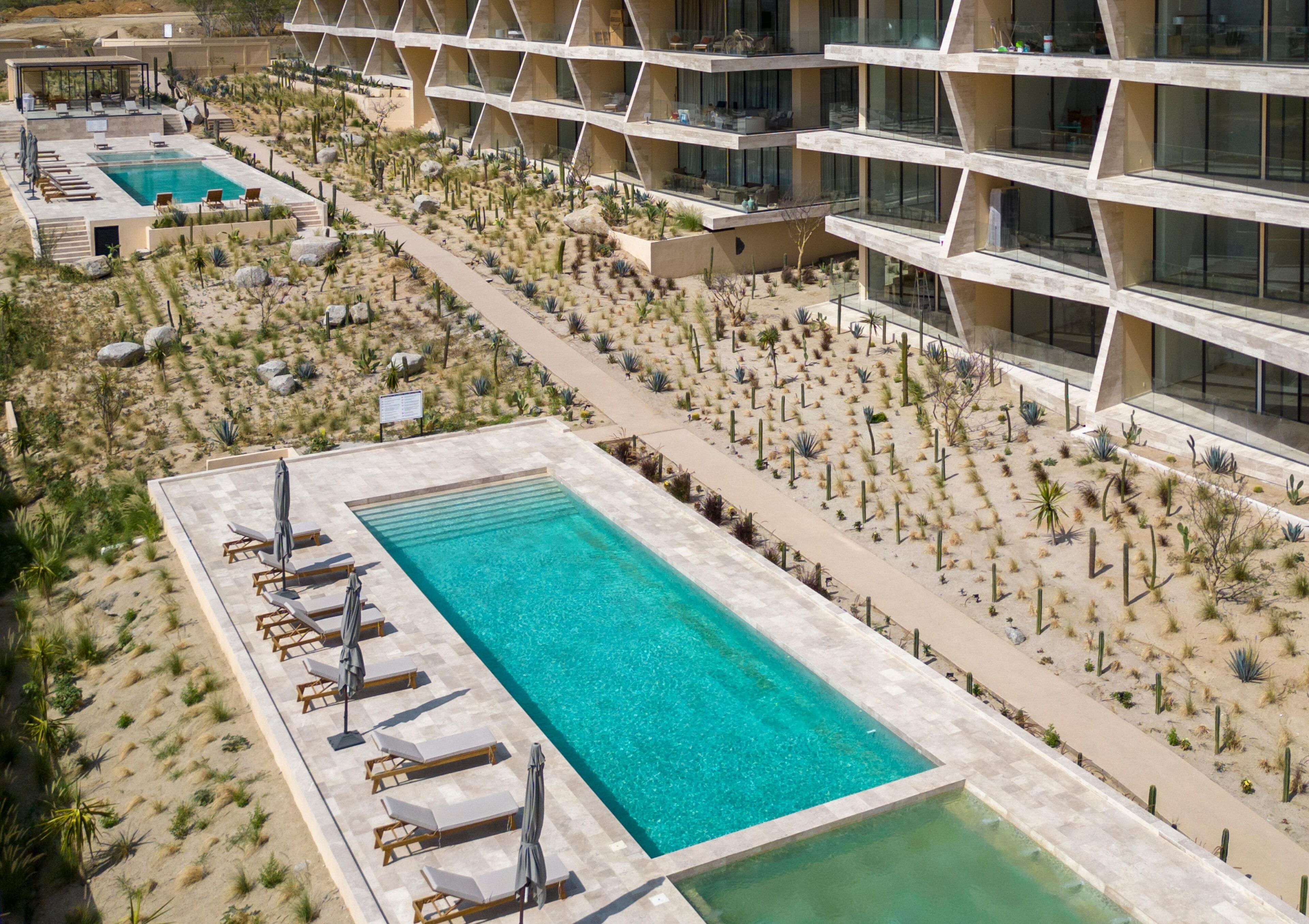 Un resort con una piscina grande, varias zonas de descanso y un jardín desértico.