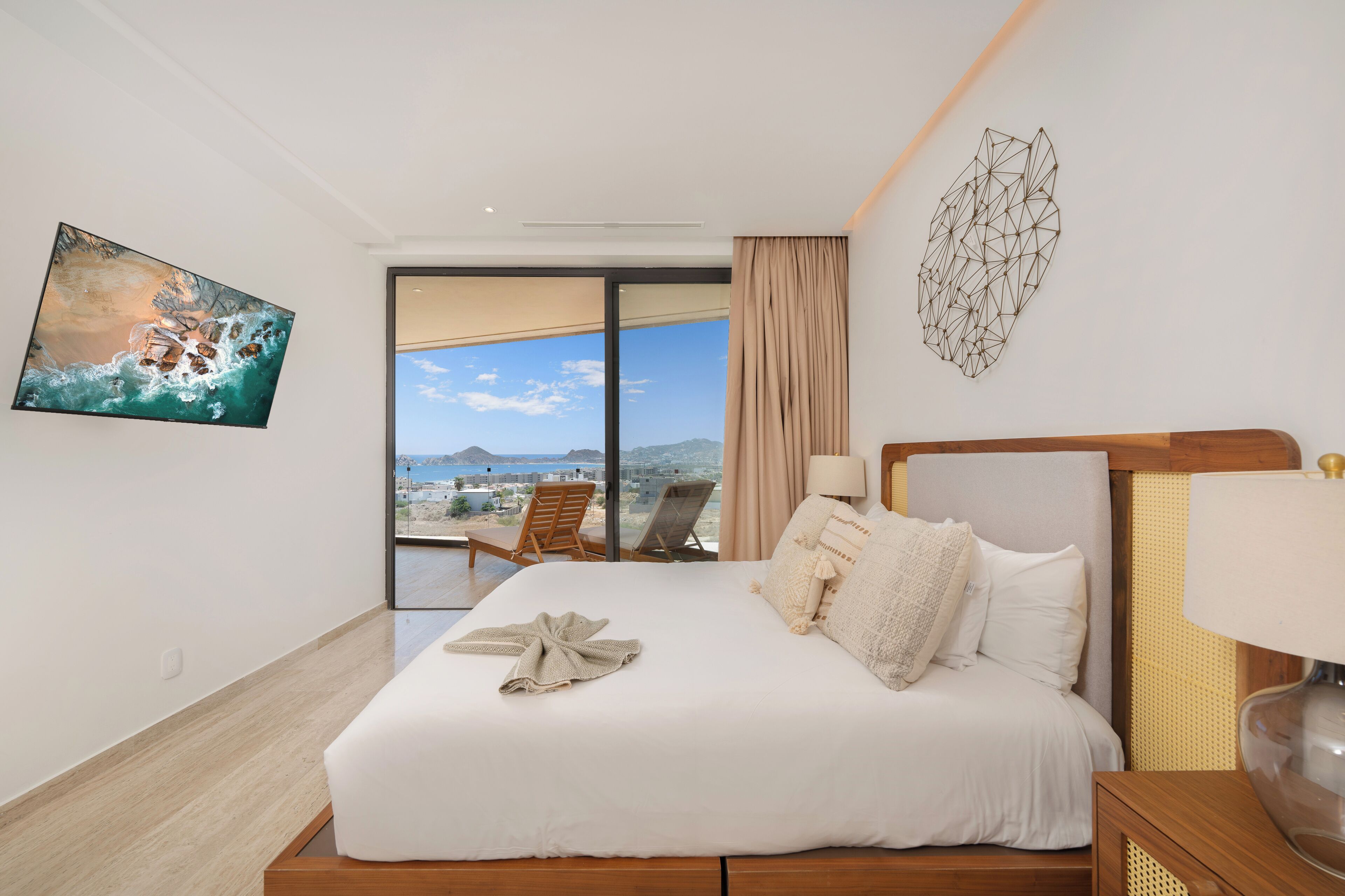 Habitación de hotel con una cama grande, vistas a la ciudad y un balcón con sillas.