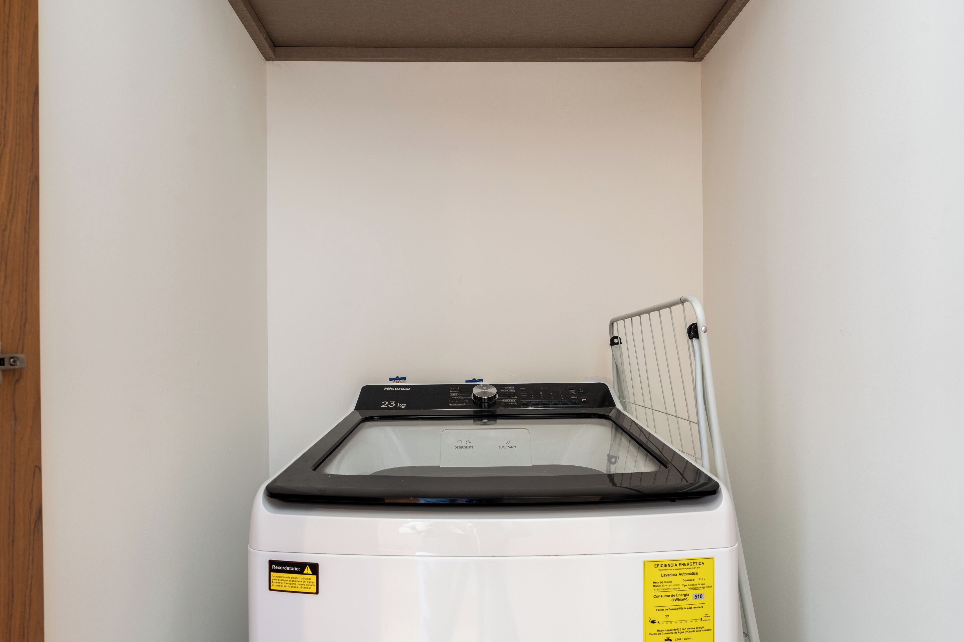 A compact, white front-loading washing machine in a small laundry room with a wooden door and a white wall.