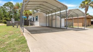 Ein überdachter Außenbereich mit Betonboden, Metallveranda und einem Holzgebäude im Hintergrund.