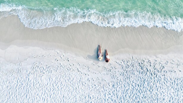 Una playa con dos personas descansando en la arena, una vista despejada del océano y una orilla arenosa.