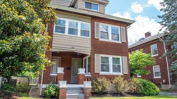A two-story brick house with a front porch, a small attached garage, and a well-maintained lawn.