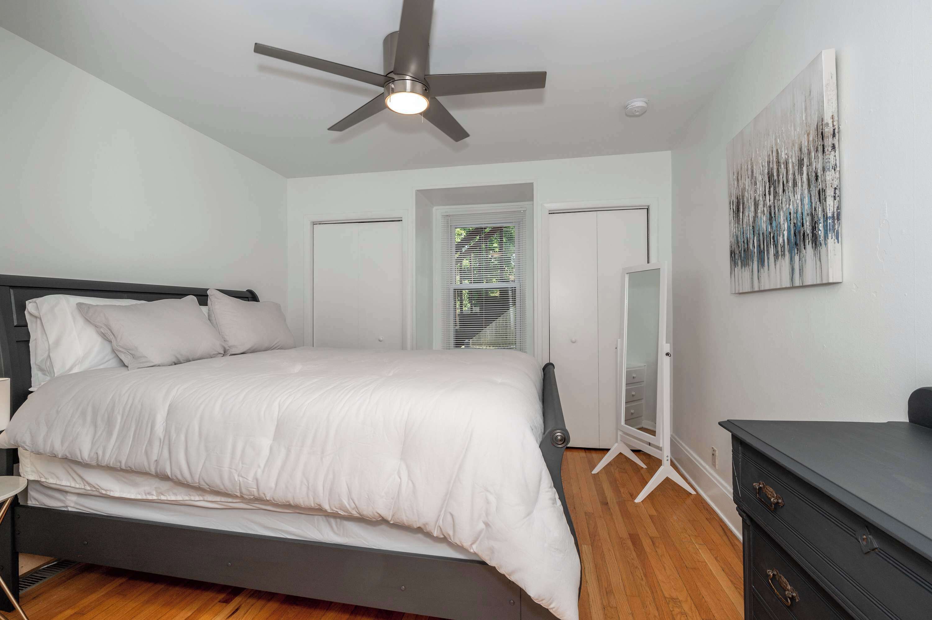 A bedroom with a bed, a ceiling fan, a dresser, and a door.