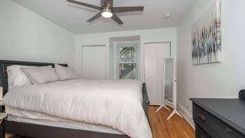 A bedroom with a bed, a ceiling fan, a dresser, and a door.