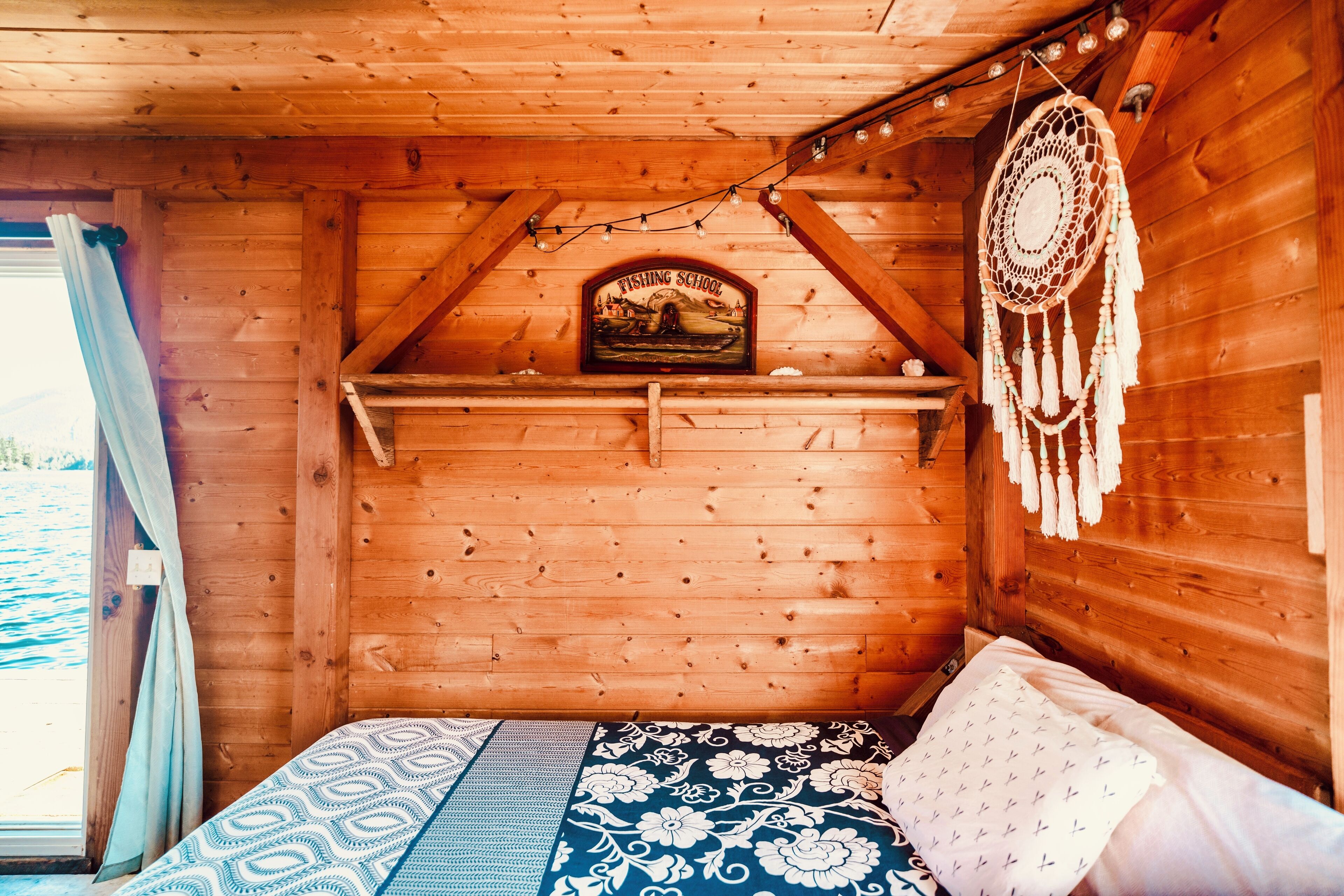 L’intérieur d’un chalet en bois, avec un lit, un attrape-rêves et un tableau encadré accroché au mur.