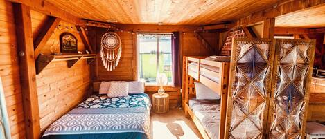 A cozy wooden cabin with a bed, a small table, and a bunk bed.