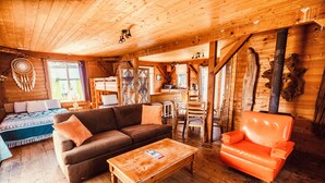 Hyggelig interiør i en træhytte med sofa, lænestol og spiseplads.