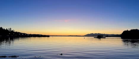 A calm lake at sunset with a boat in the distance and a forested shoreline.