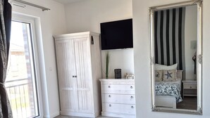 Een slaapkamer met een bed, een kledingkast, een dressoir, een spiegel en een raam met gordijnen.