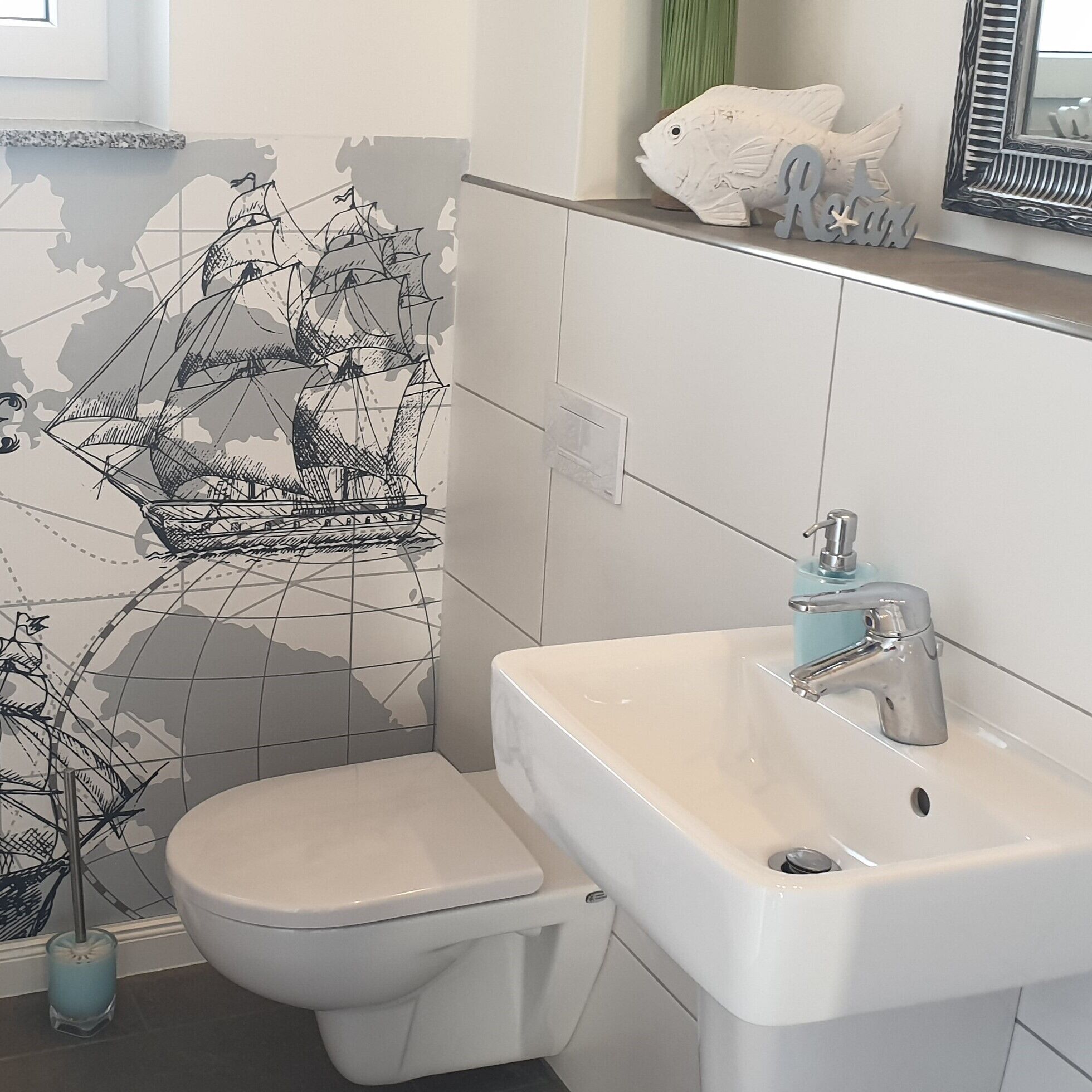 A bathroom with a white toilet, a sink with a modern faucet, and a decorative ship mural on the wall.