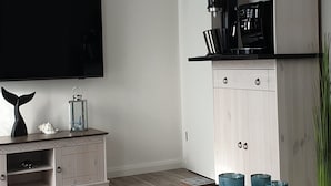 Een moderne woonkamer met een flatscreen televisie, een houten kast met keukenapparatuur, en een koffieapparaat.