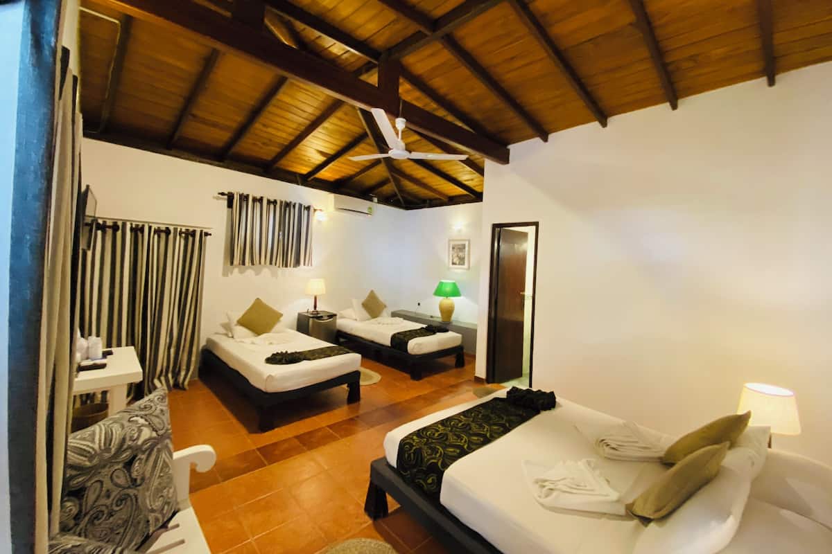 Habitació d'hotel amb sostre de fusta, dos llits, una taula petita, una cadira i una porta.