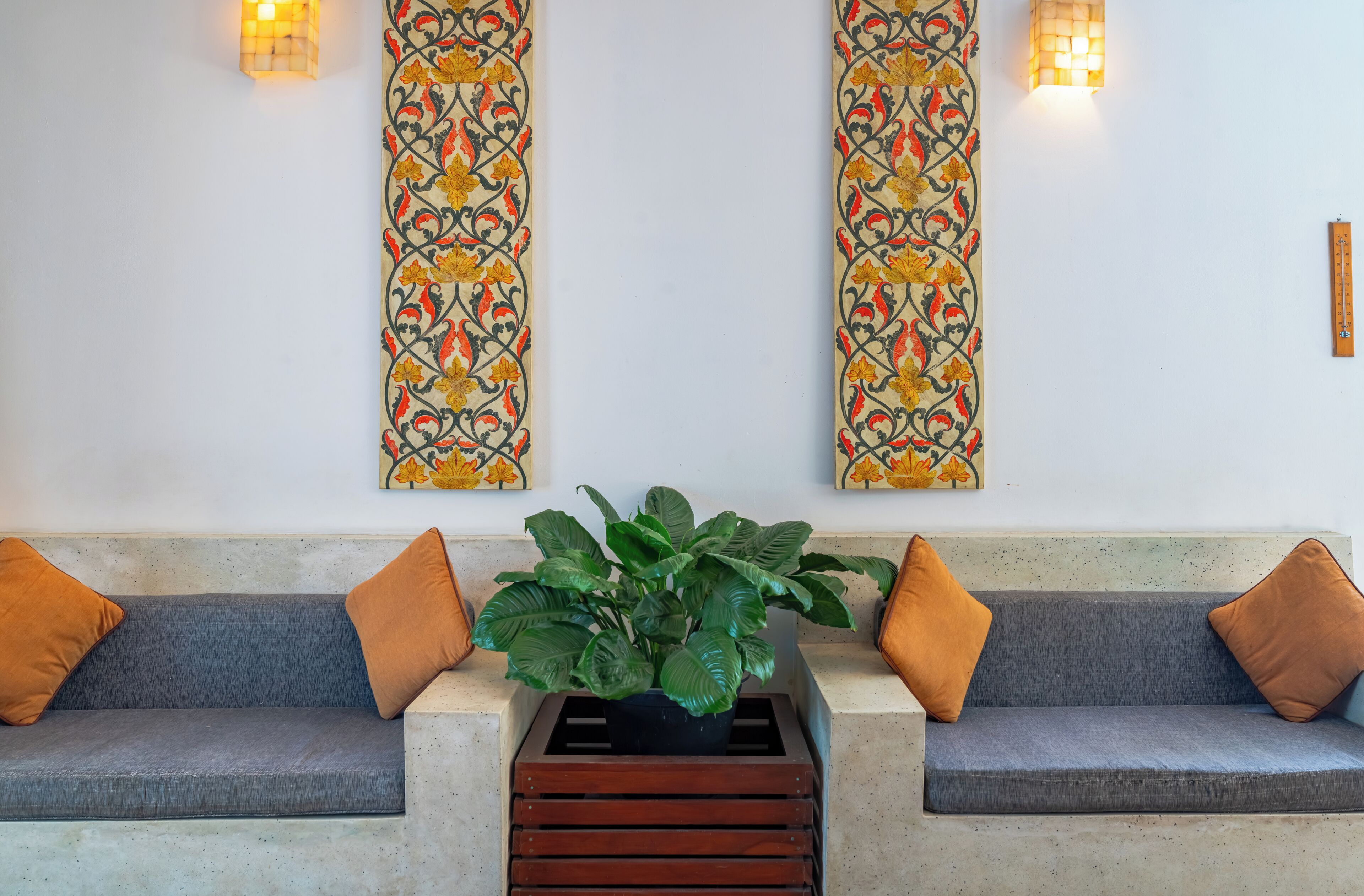 A sofa with two brown cushions, a potted plant, and a decorative wall panel with a light fixture.