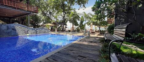 A wooden deck with a swimming pool, surrounded by trees and outdoor furniture.