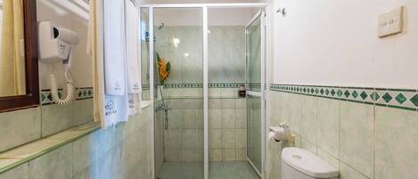 A bathroom with a toilet, a glass-enclosed shower, a hairdryer, and a towel rack.