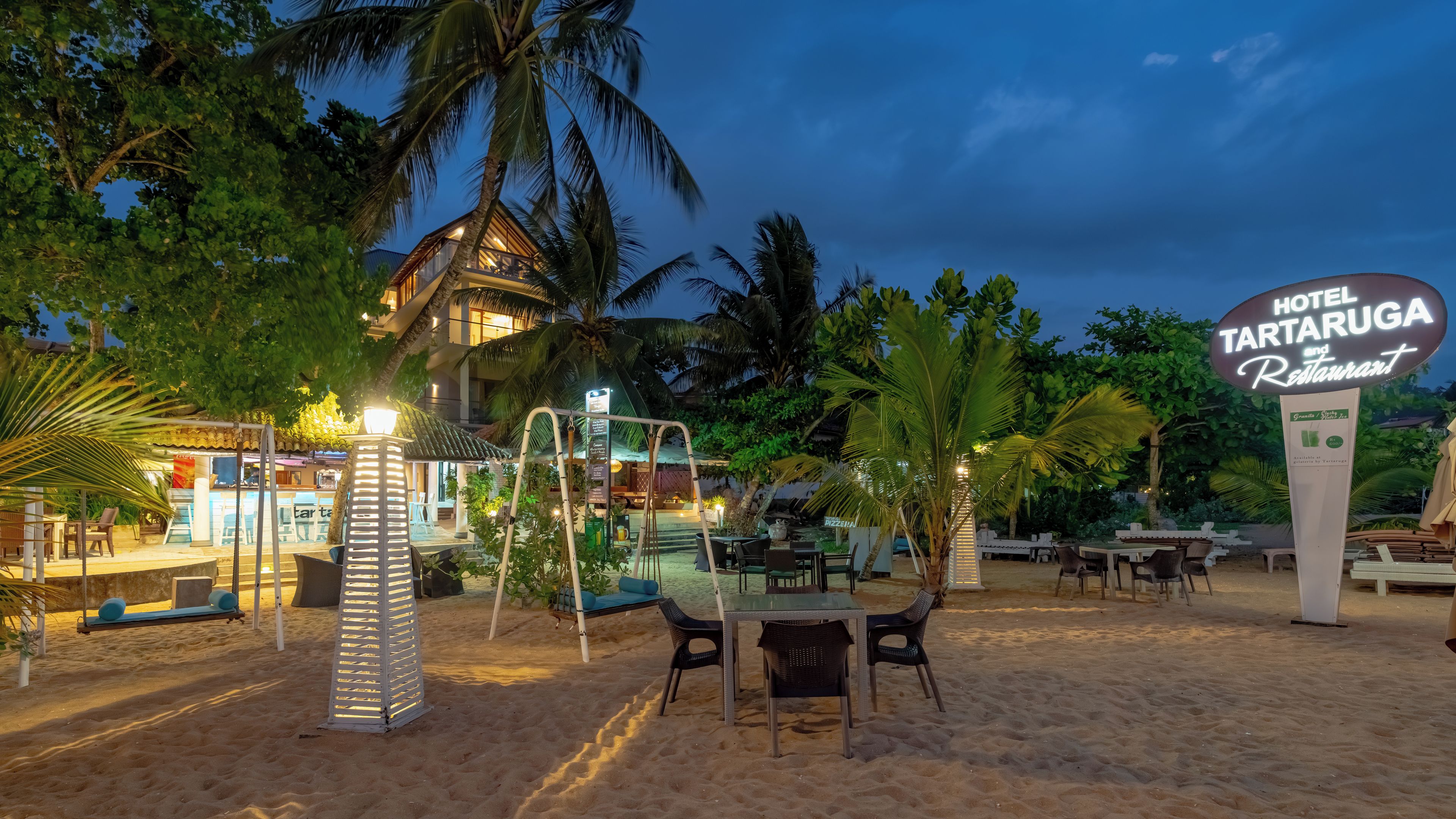 A beachfront hotel with outdoor seating, palm trees, and a sign for the hotel and restaurant.