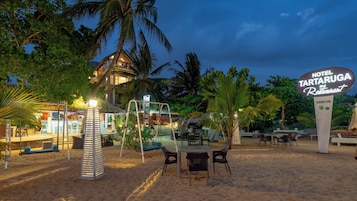 A beachfront hotel with outdoor seating, palm trees, and a sign for the hotel and restaurant.