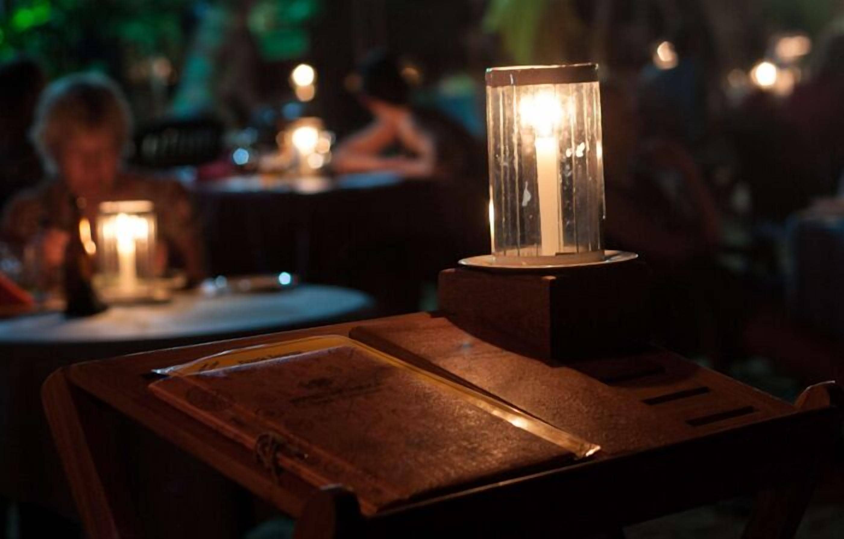 A candlelit table with a menu and a clear glass candle holder.
