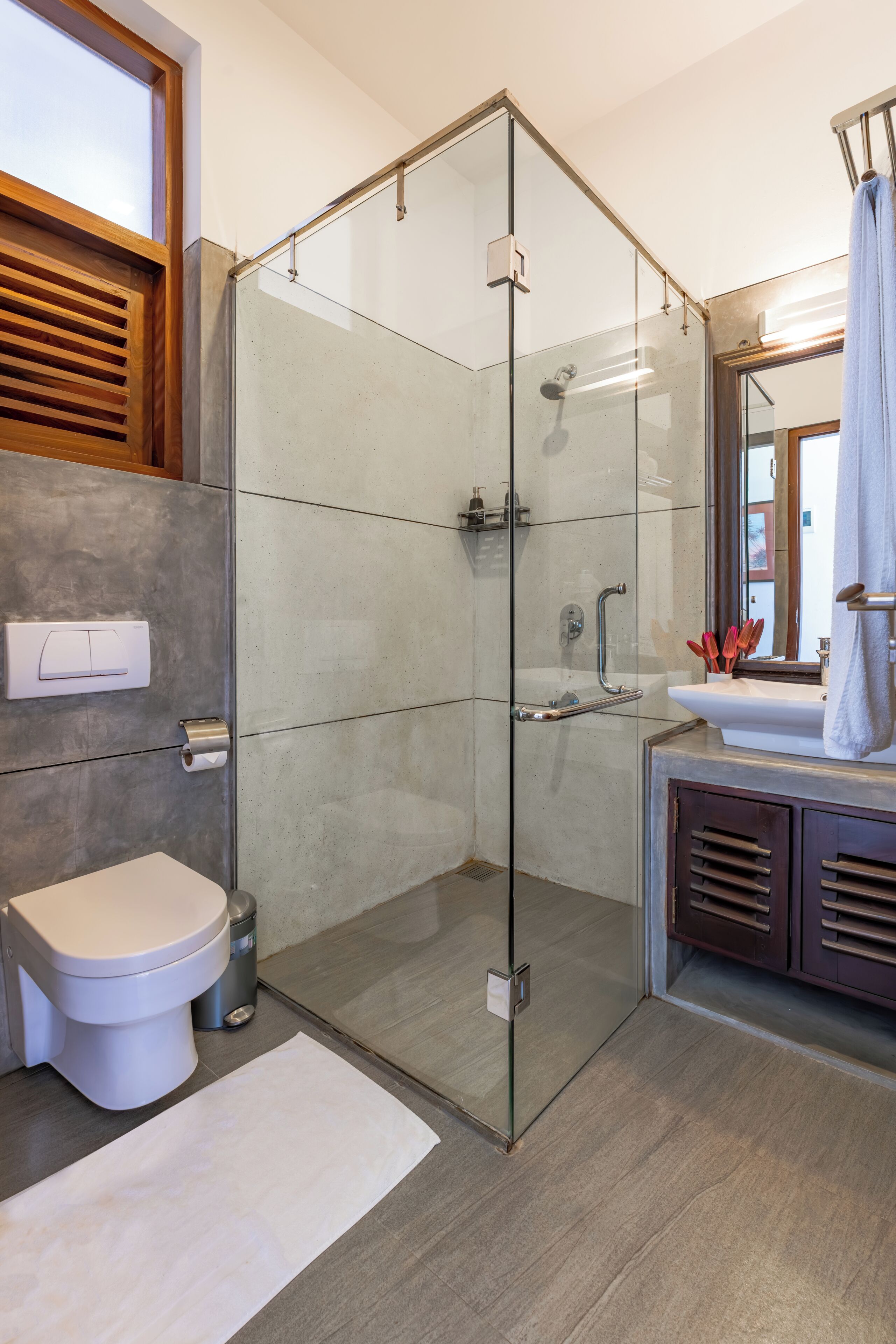 A modern bathroom with a glass-enclosed shower, a white toilet, a sink with a mirror, and a wooden vanity.