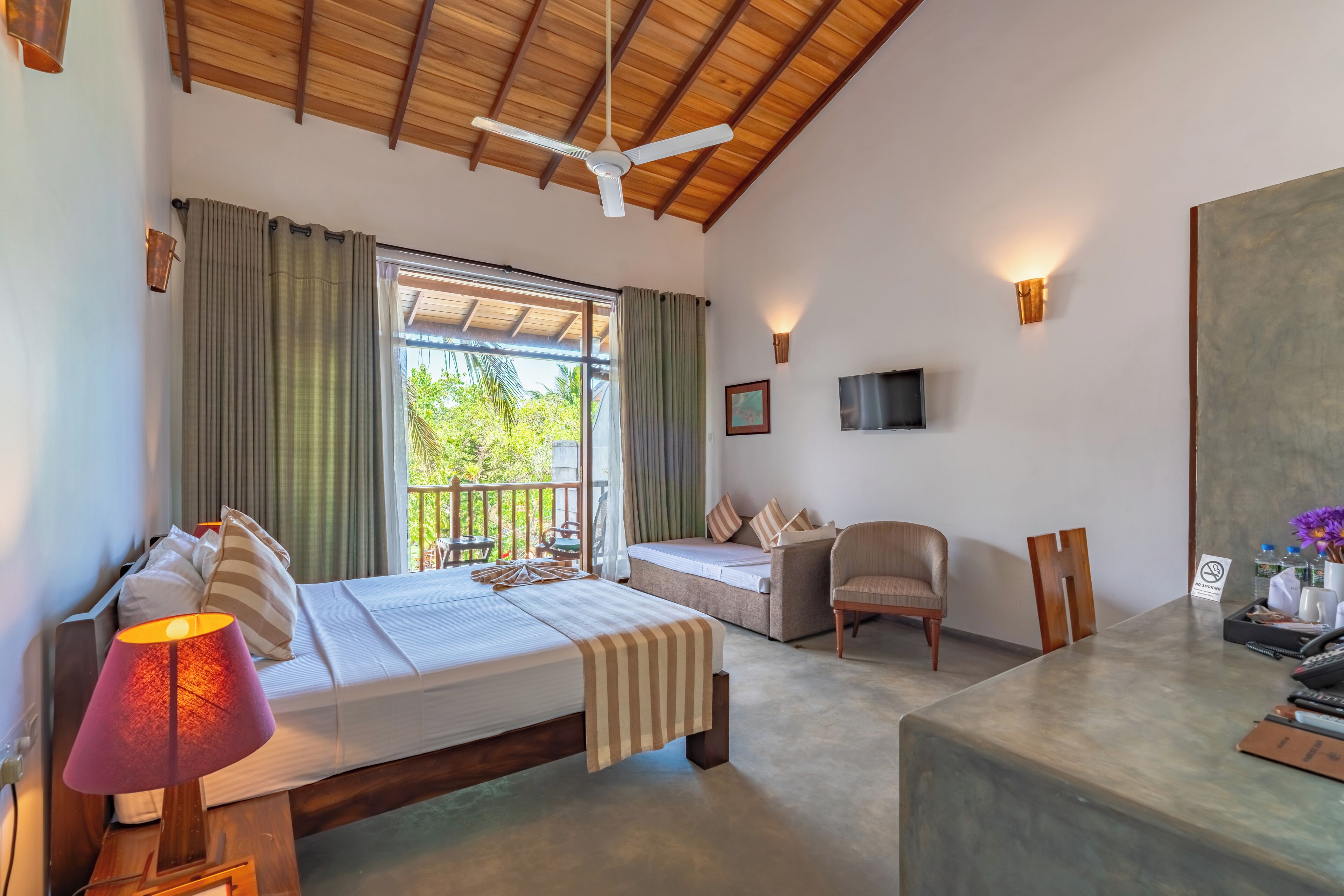 A bedroom with a bed, a desk, a chair, a TV, and a balcony with curtains.
