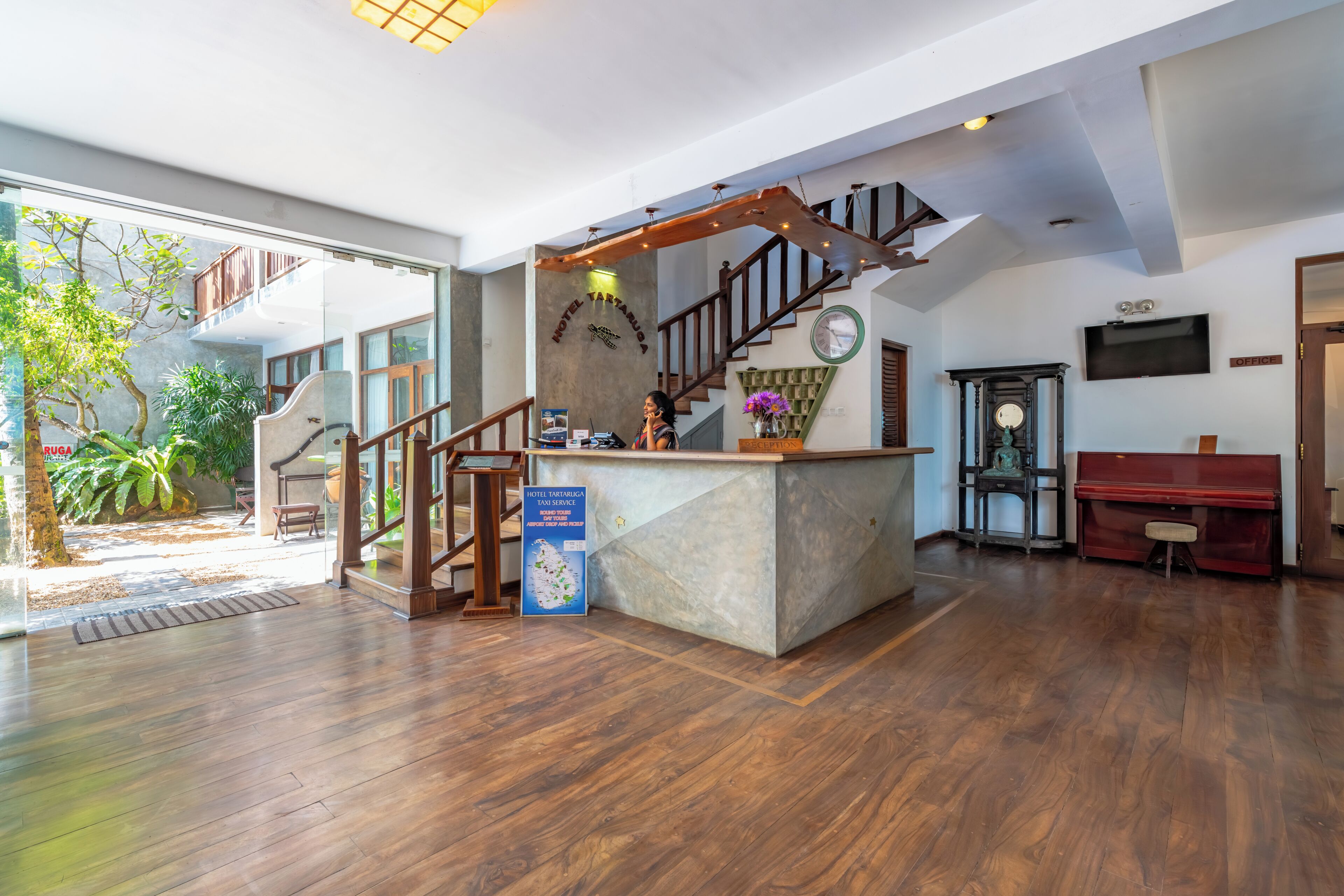 A hotel lobby with a reception desk, a staircase, a piano, and a clock.