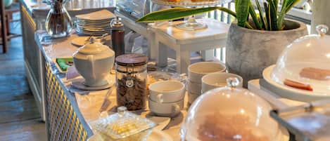 Disposição de buffet com diversos alimentos, um espaço para café e uma planta decorativa.