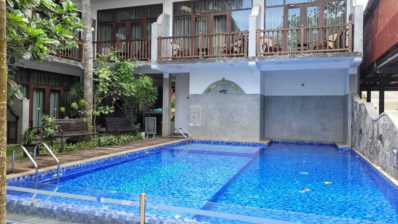 A hotel with a swimming pool, a balcony with seating, and a sign indicating the hotel name.