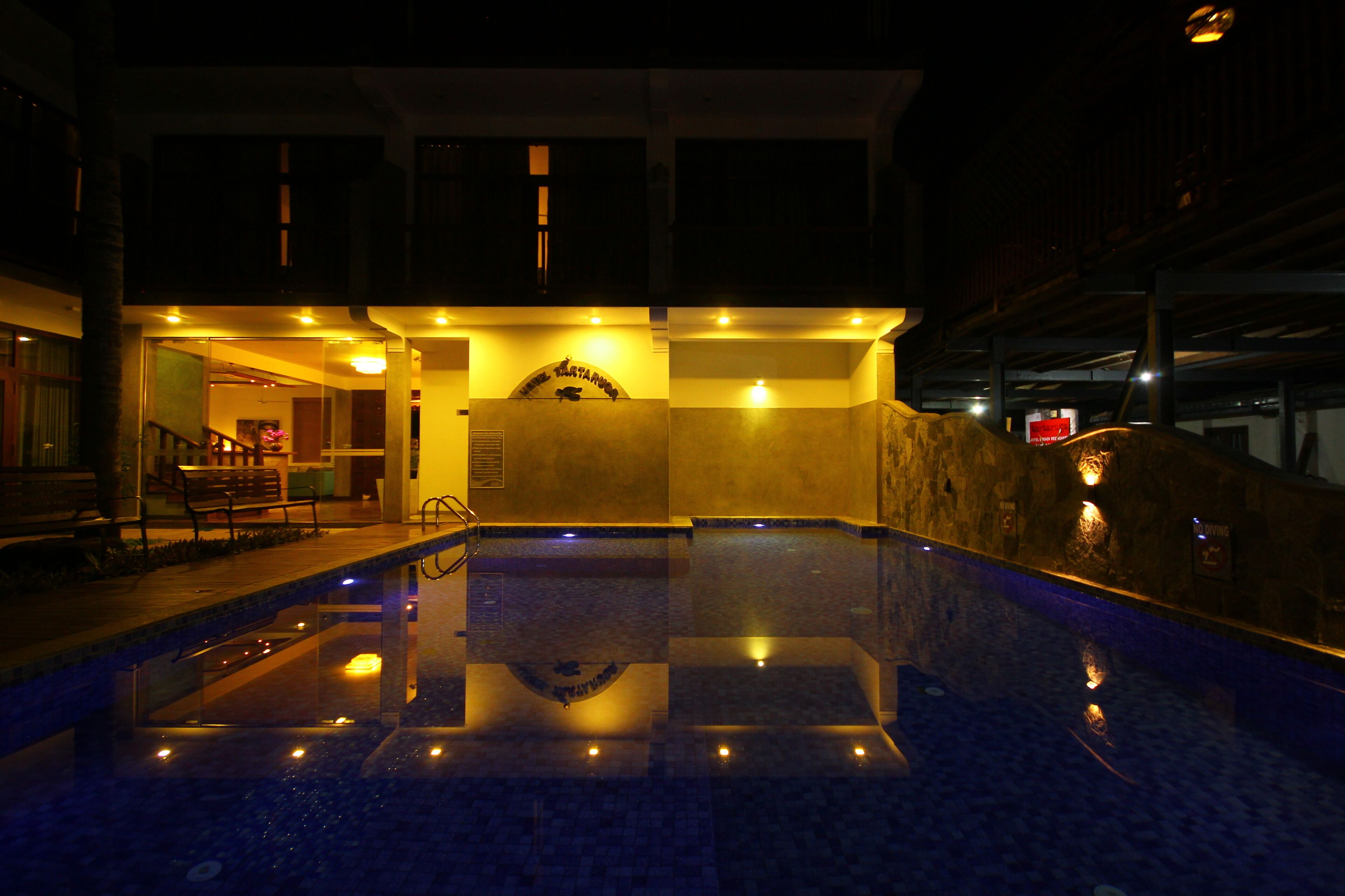 A nighttime view of a swimming pool area with a stone wall and a sign above the pool.