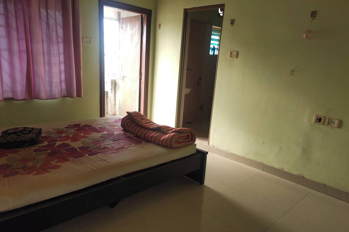 Una habitación con cama, ventana con cortinas, una puerta y un enchufe.